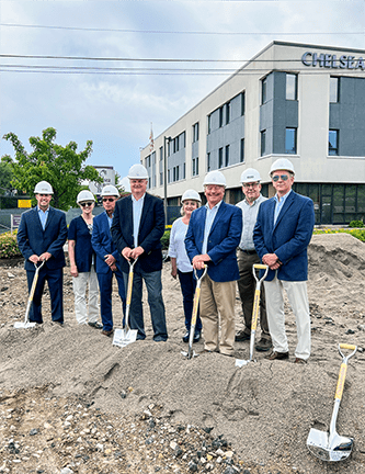 6 men and 2 women in blue blazers and white construction hats holding shovels and standing on a pile of dirt outside of Averon Trust Bank