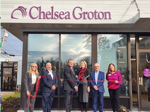 3 men and 3 women in business attire hold a red ribbon in front of Averon Trust Bank